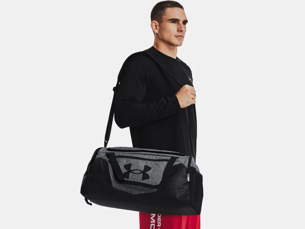Sac Sport - Under Armour noir et gris en tissu résistant, porté à l'épaule par homme adulte, vue latérale.